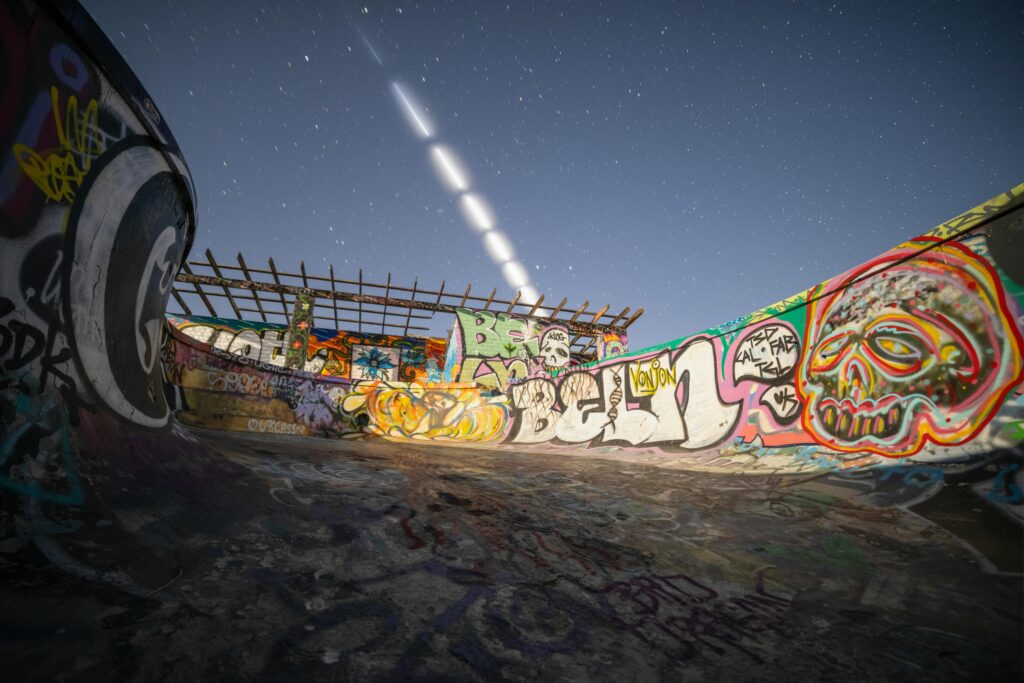Dynamic view of a graffiti-covered skate park under a starry night sky with light trails.