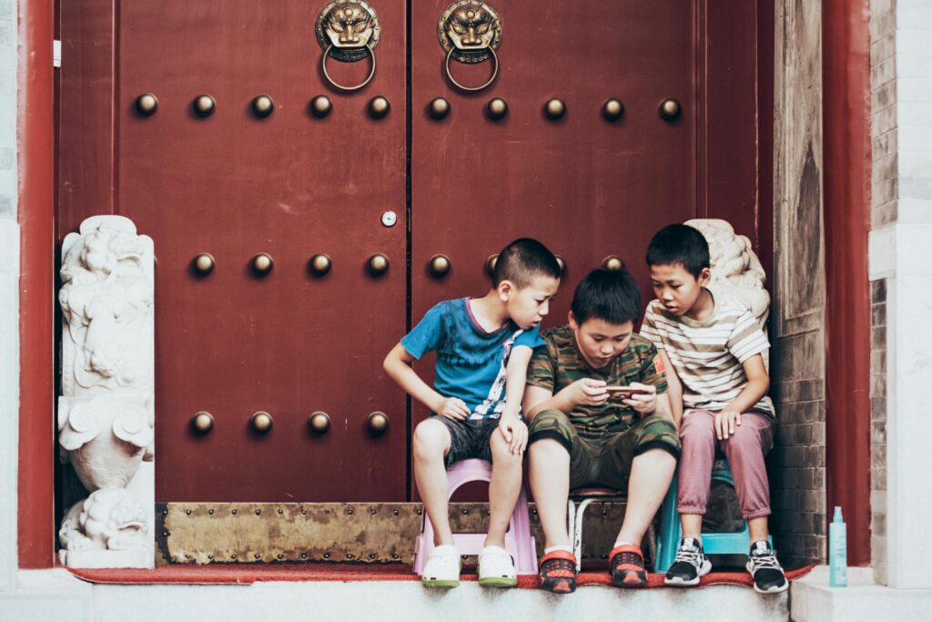 Three young boys sitting outdoors, engrossed in mobile games on a temple step in Beijing.