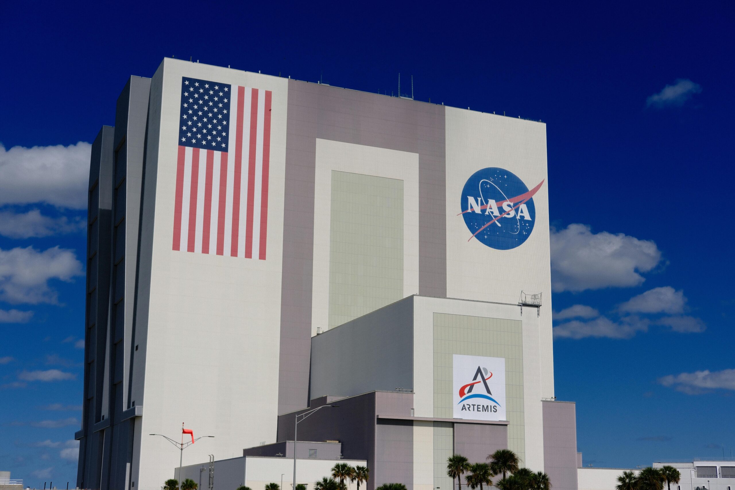 The iconic NASA Vehicle Assembly Building at Kennedy Space Center in bright daylight.