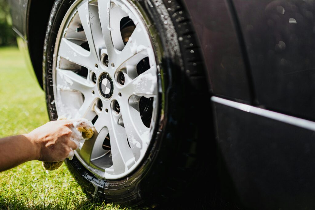 Detailed shot of a car wheel being cleaned at home in a sunny outdoor setting.