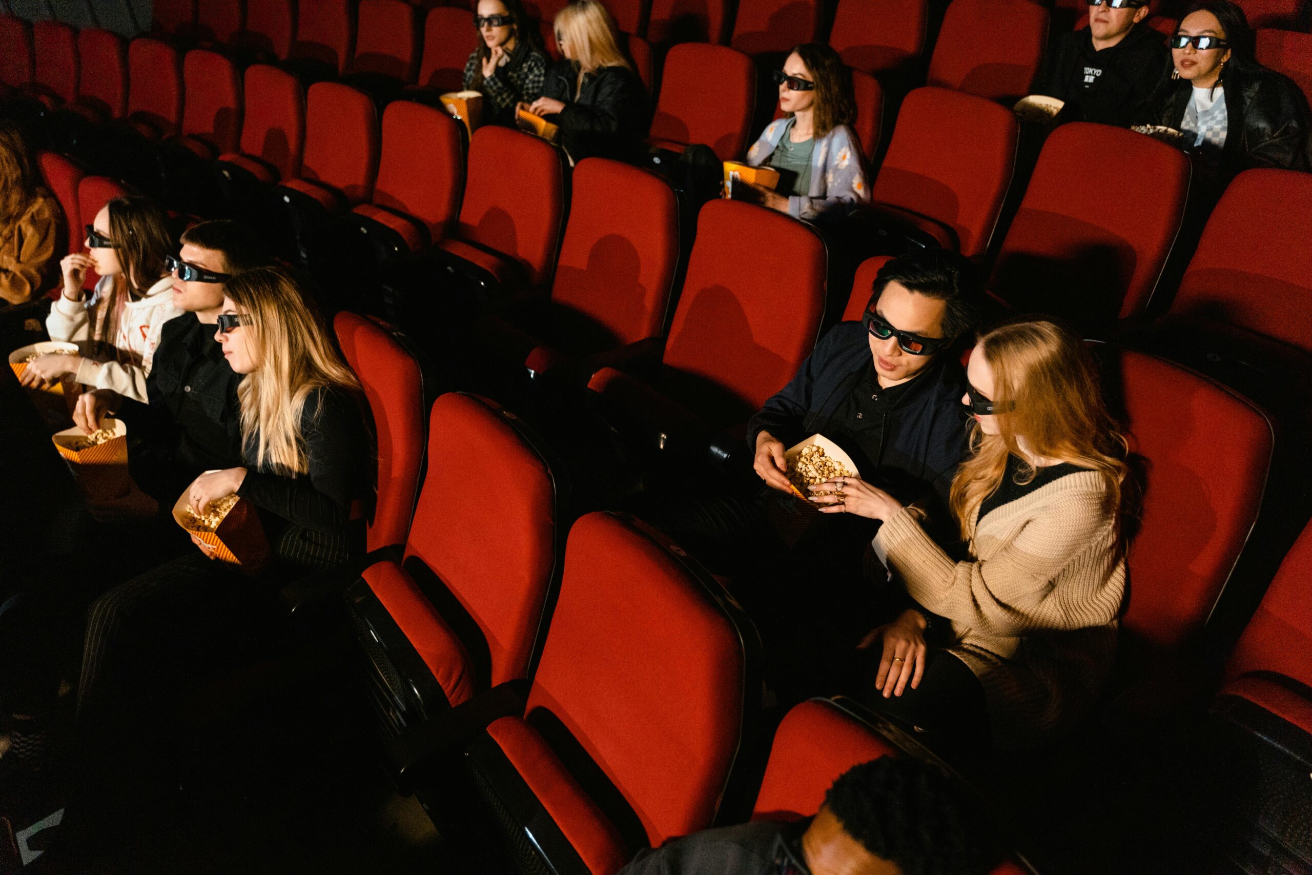 People in a theater wearing 3D glasses watching a movie with popcorn.