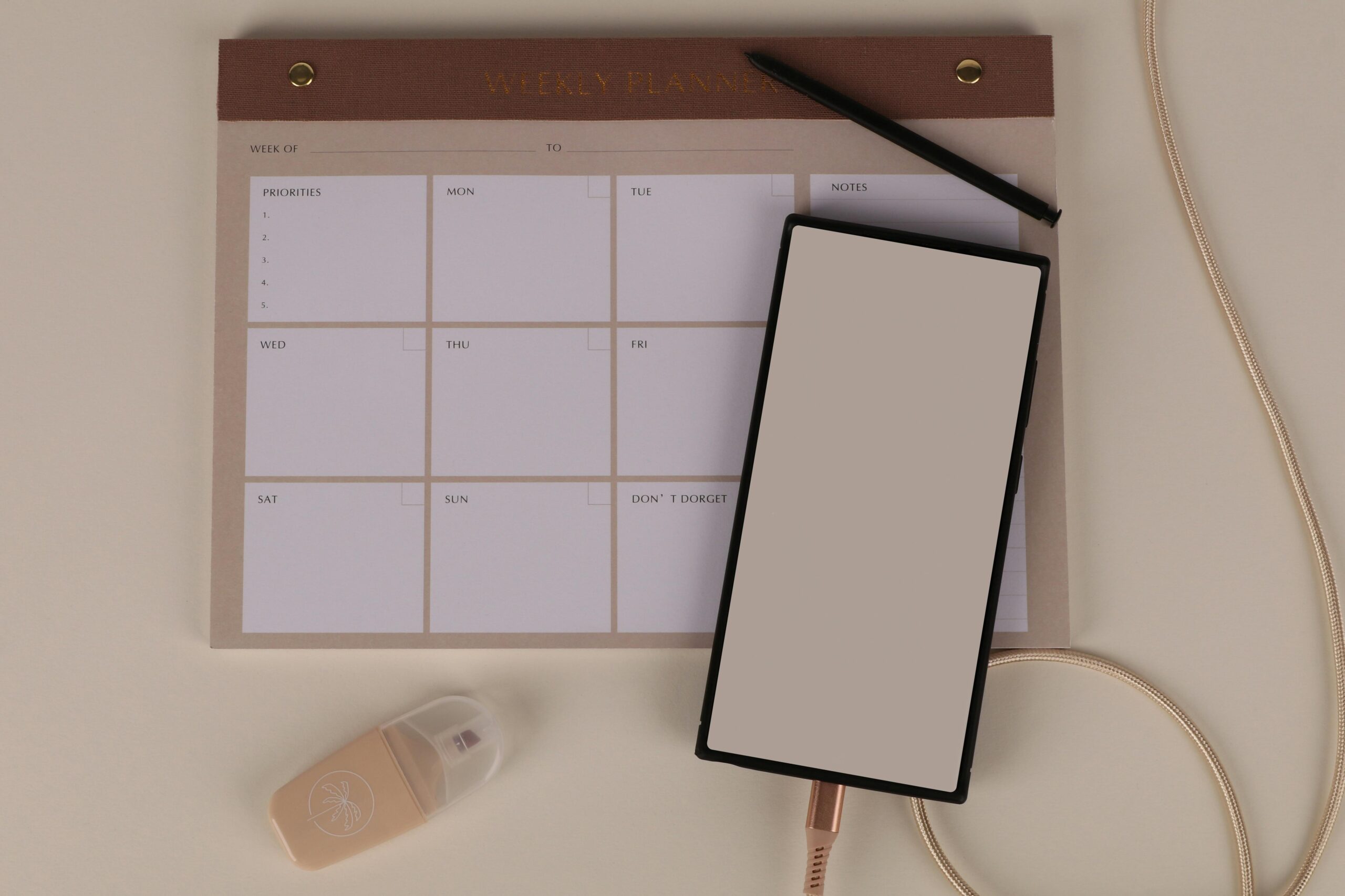 Flat lay of a minimalist desk setup featuring a weekly planner, smartphone, and stationery.