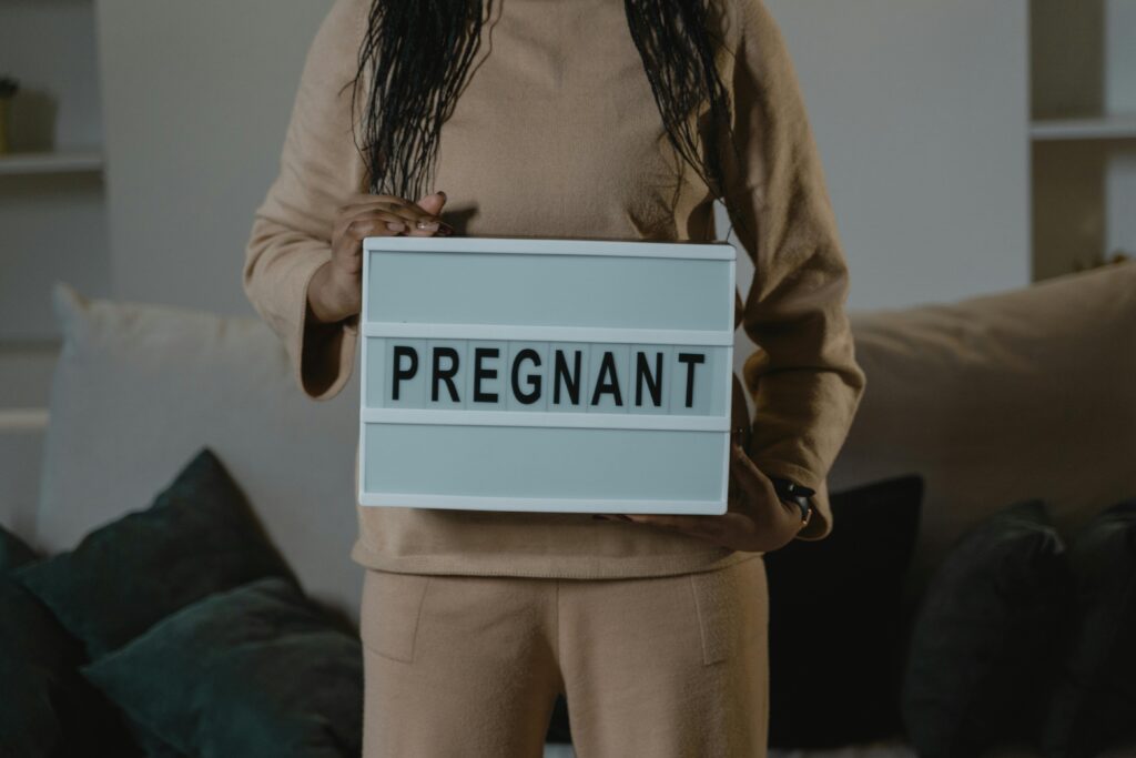 A woman in beige holds a lightbox with 'PREGNANT' indoors. Expectant motherhood concept.