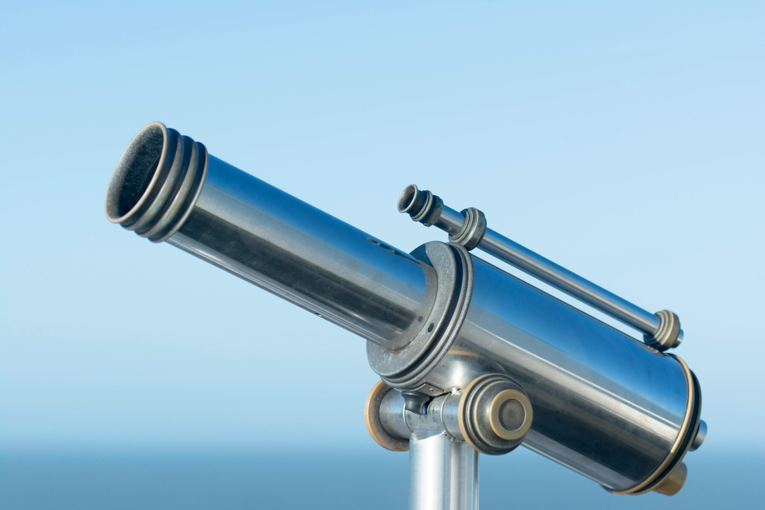 A sleek metallic coin-operated telescope pointing into a clear blue sky, perfect day for sightseeing.