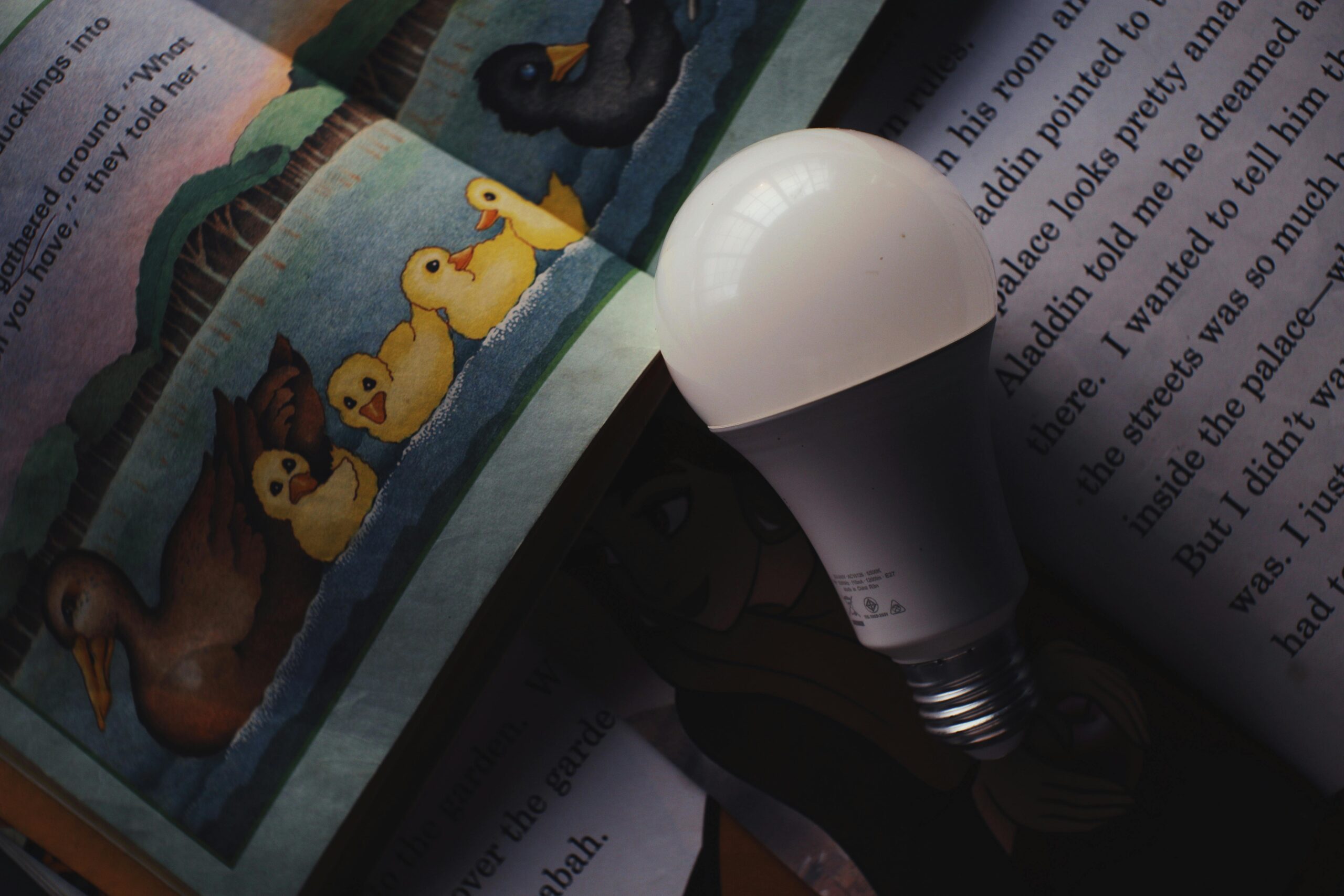 A light bulb placed on an open book with colorful illustrations, showcasing imagination and learning.