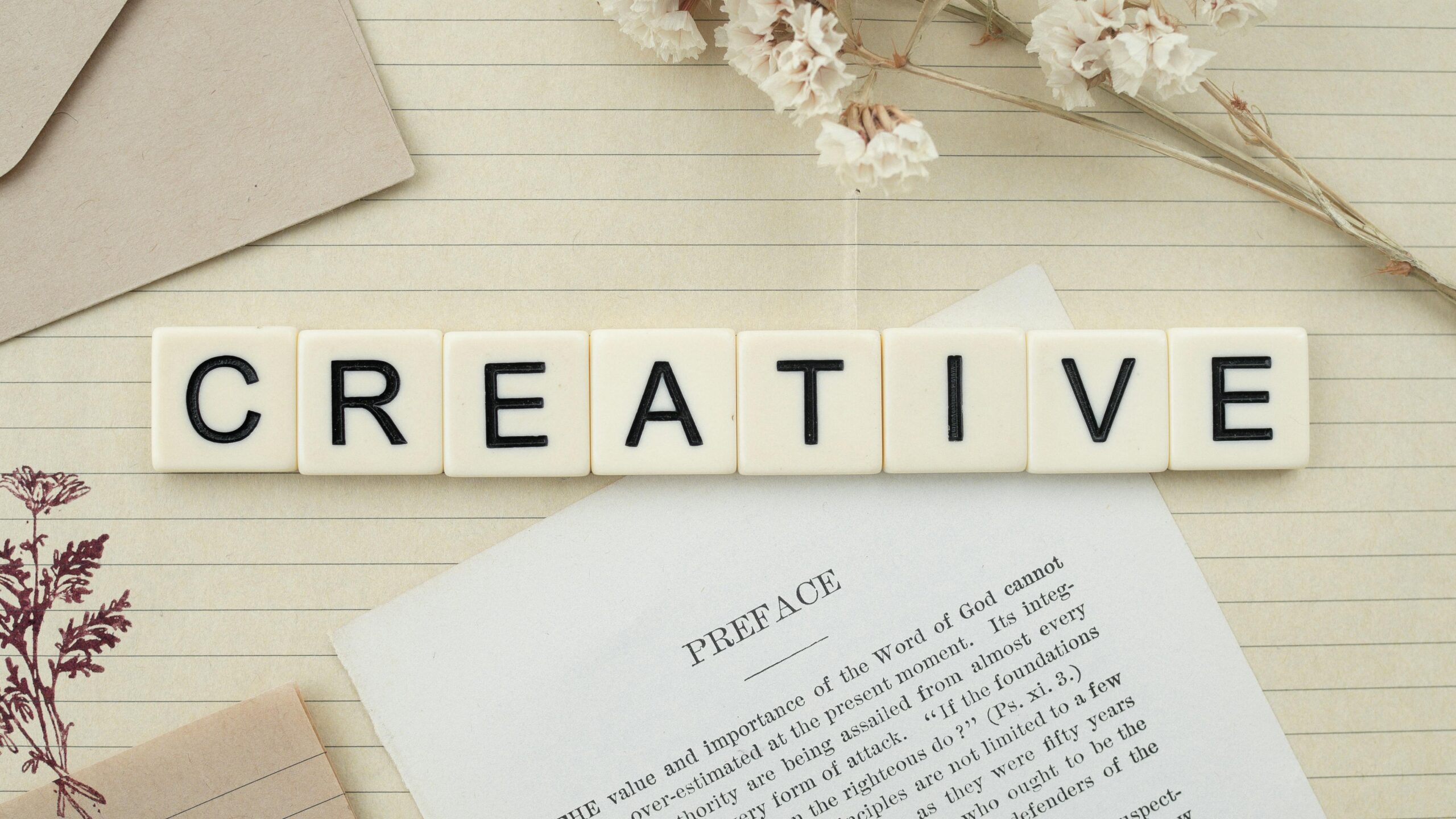 Close-up of letter tiles spelling 'Creative' on a lined notepad with decorative elements.